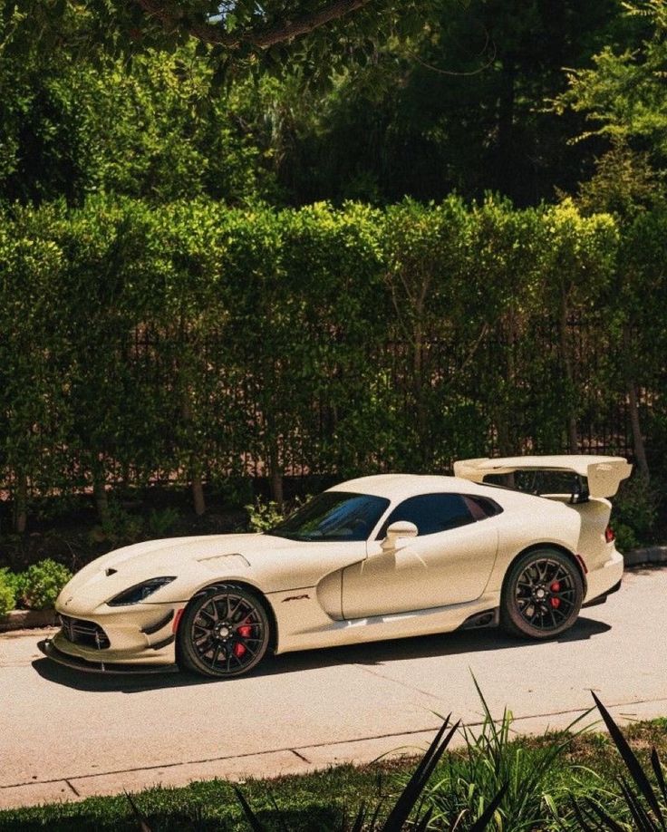 a white sports car is parked on the side of the road in front of some bushes