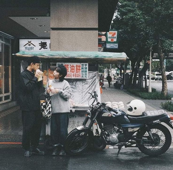 a man and woman standing next to a motorcycle