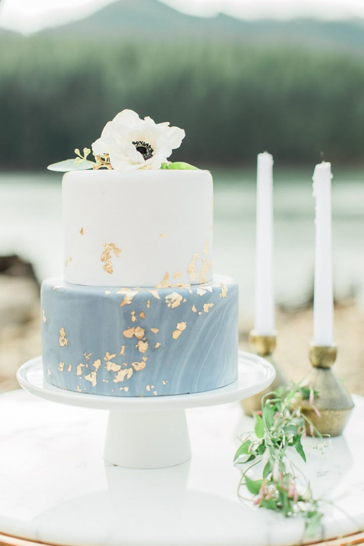 a blue and white wedding cake sitting on top of a table next to two candles