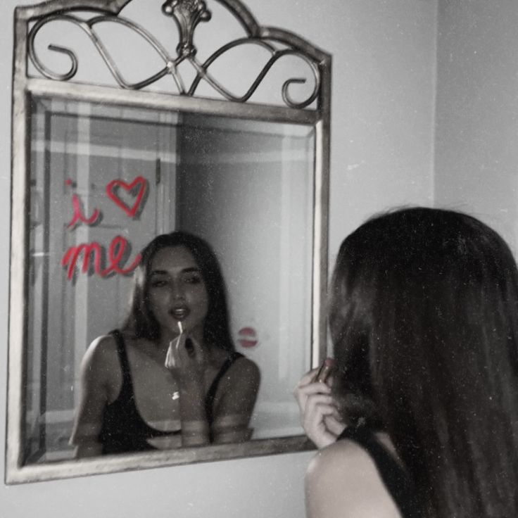 a woman brushing her teeth in front of a mirror with writing on the wall behind it