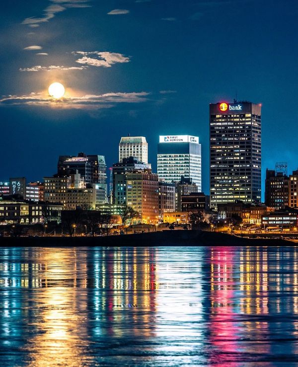 the full moon shines brightly in the city skyline as it reflects on the water