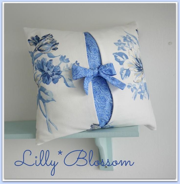 a blue and white pillow with a bow on the front is sitting on a shelf