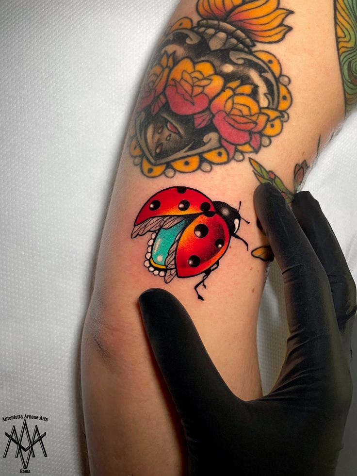 a ladybug tattoo on the arm of a person with black gloves and tattoos