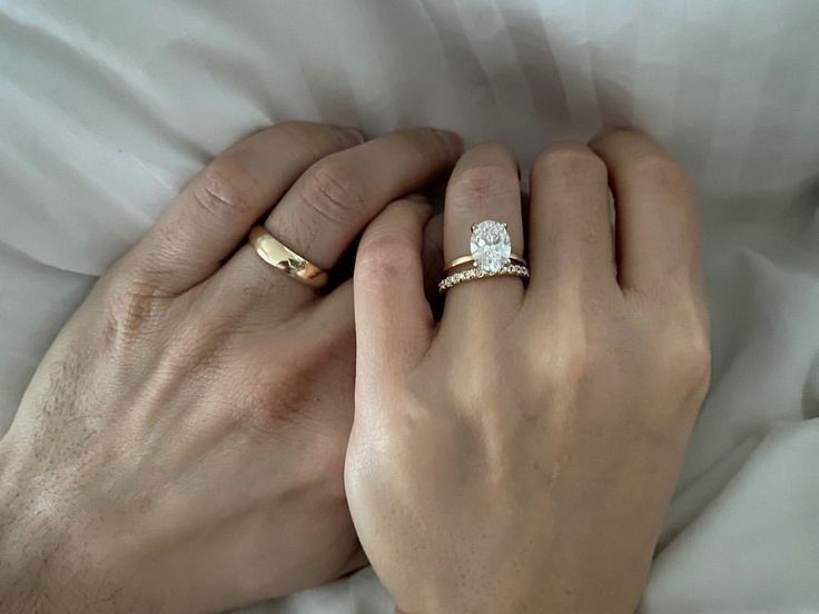 a man and woman holding hands on top of a white sheet with two gold rings