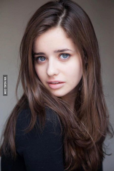 a woman with long brown hair and blue eyes is posing for a photo in front of a gray background