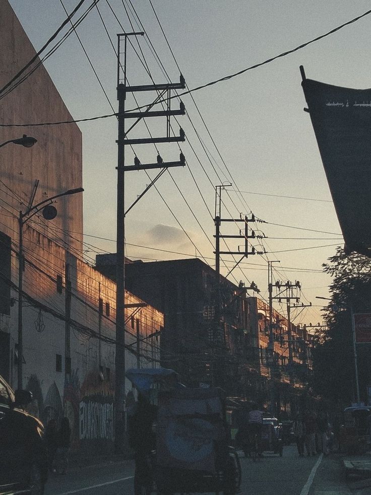 cars and people are driving down the street in front of tall buildings with power lines above them