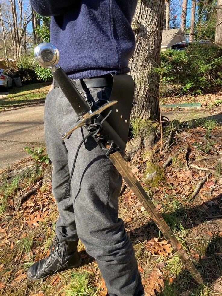 a person standing in front of a tree with two swords attached to their back legs