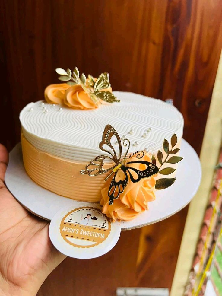 a person holding up a cake decorated with flowers and butterflies on the top of it