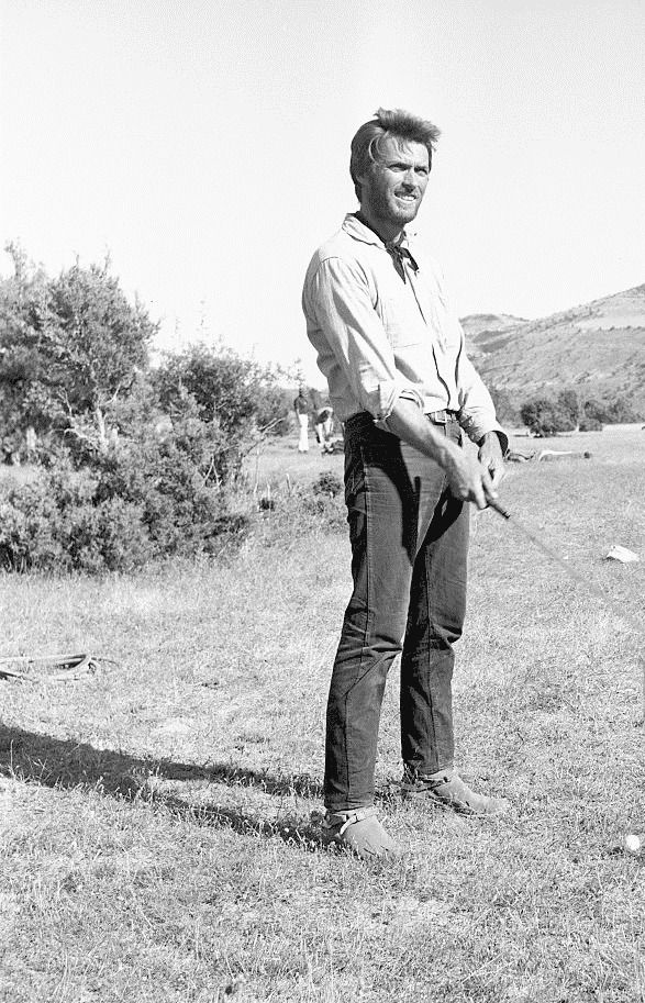 a man standing in the grass holding a baseball bat and looking off into the distance