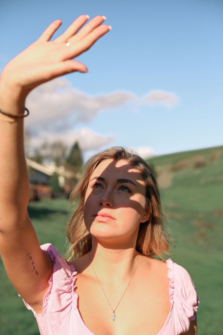 a woman in a pink top is holding her hand up to the sky with one hand