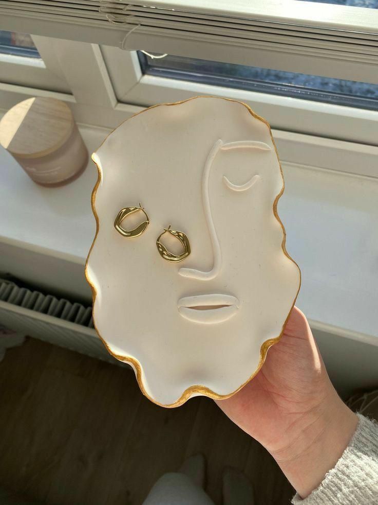 a person holding up a face shaped plate with two gold wedding rings on top of it