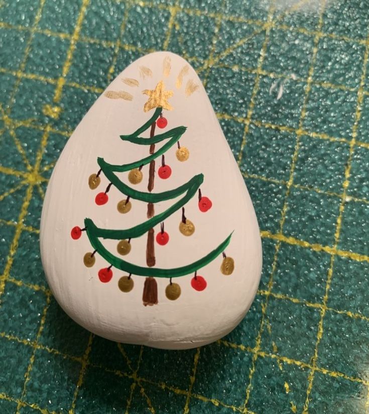 a painted rock with a christmas tree on it sitting on a green tableclothed surface