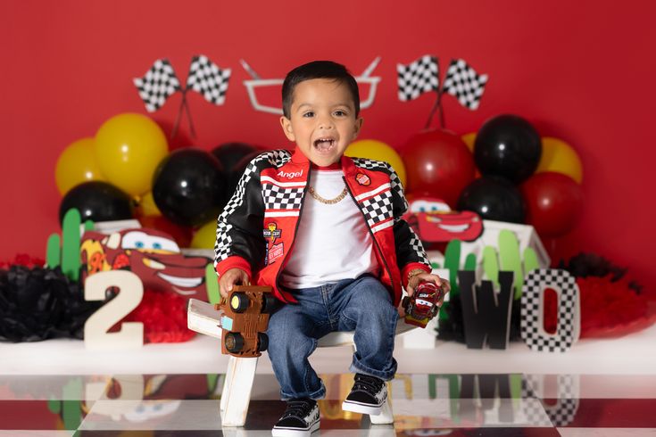 a young boy sitting on top of a wooden chair in front of a red wall