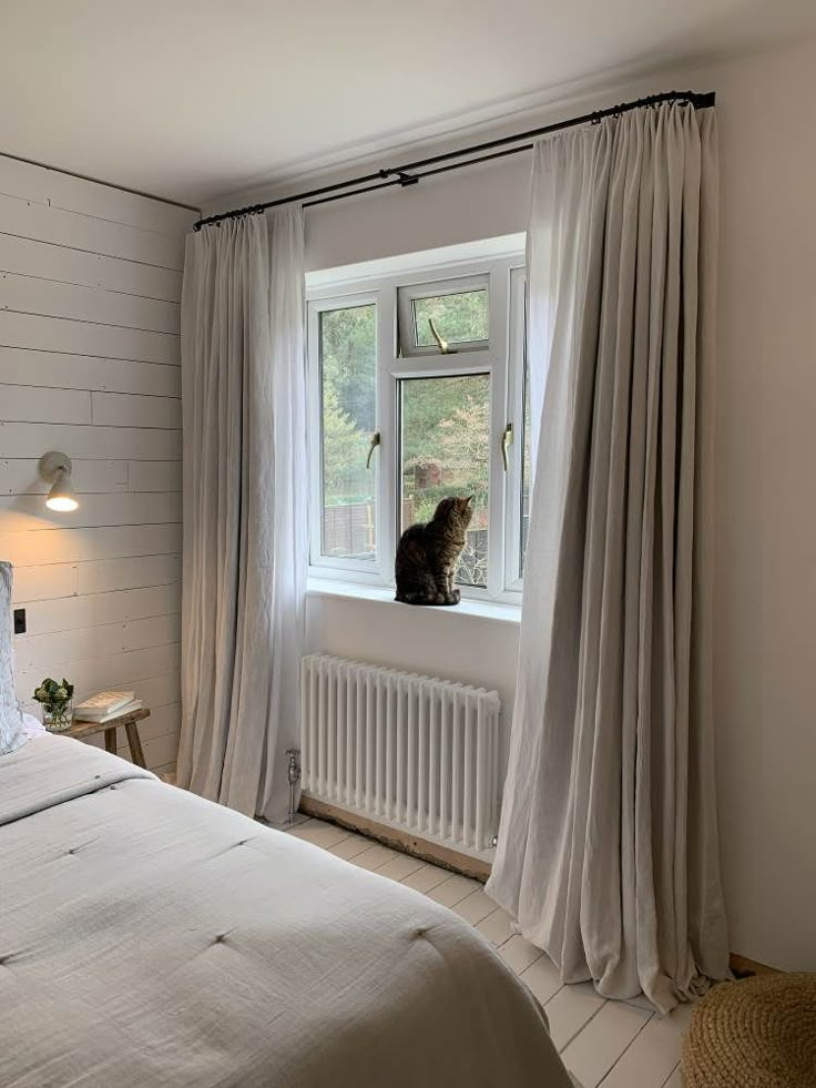 a cat sitting on top of a window sill next to a bed in a bedroom