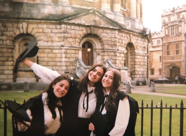 three young women posing for a photo in front of a building with a gate and iron fence