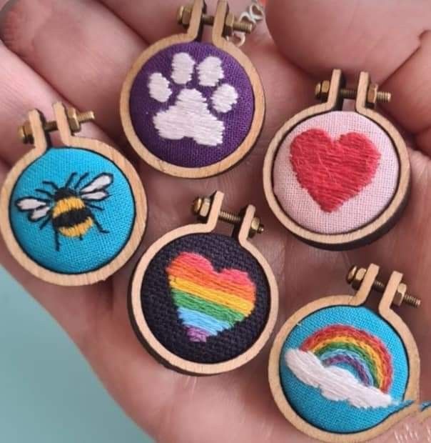 the hand is holding six embroidered badges with hearts, rainbows, and a bee