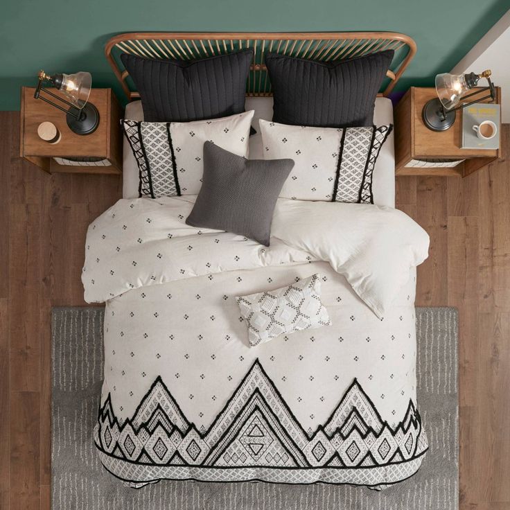 a bed with black and white pillows on top of it next to a night stand