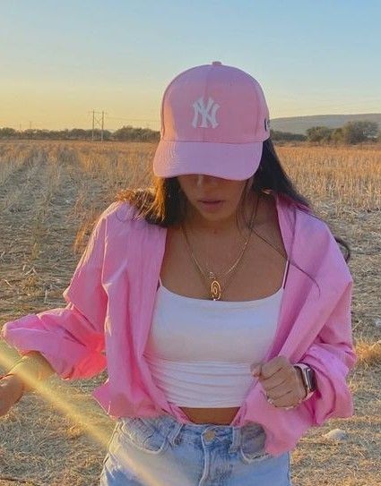 a woman wearing a pink hat and jacket in an open field with her hands on her hips