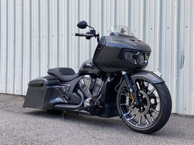 a black motorcycle parked in front of a metal building with a white wall behind it