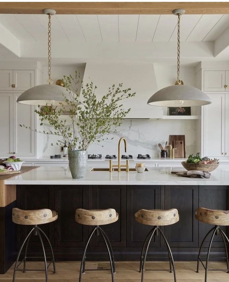 three stools sit in front of a kitchen island with marble counter tops and pendant lights