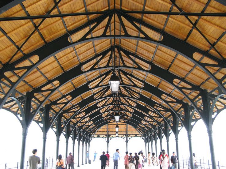 many people are walking around in a covered area with wood roofing and metal beams