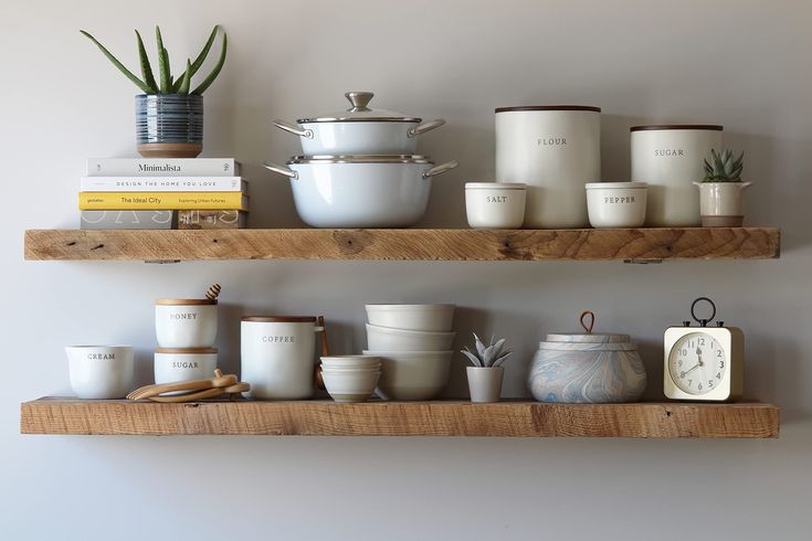 two wooden shelves with pots and pans on them next to a wall mounted clock