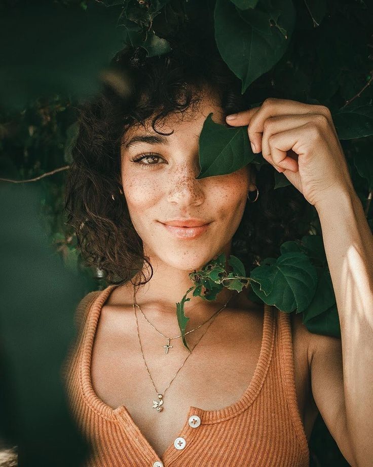 a woman is smiling while holding onto a green leaf and wearing an orange tank top