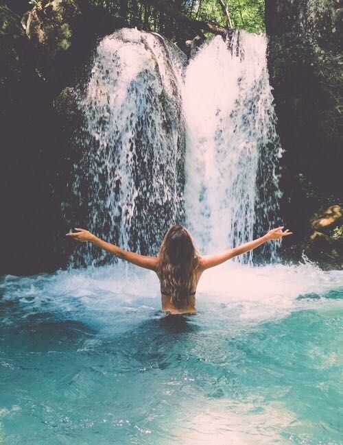 a woman standing in the water with her arms spread out and waterfall behind her back