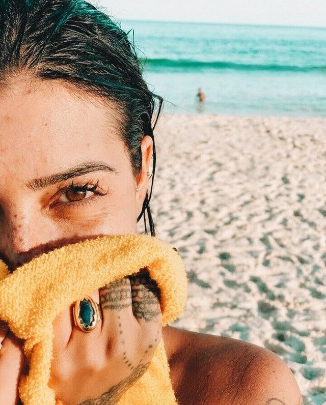 a woman covers her face with a towel on the beach while looking at the camera