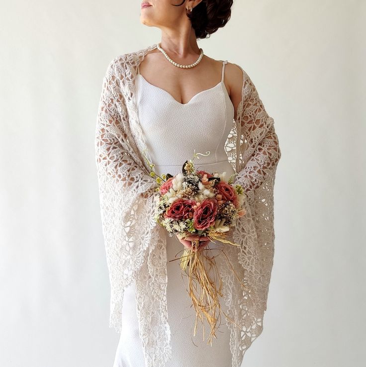 a woman wearing a white dress holding a bouquet of flowers and a shawl over her shoulders