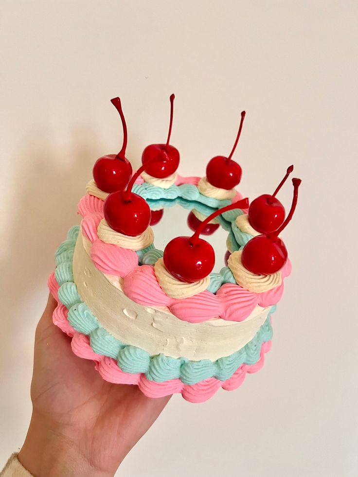 a hand holding a cake with cherries on top