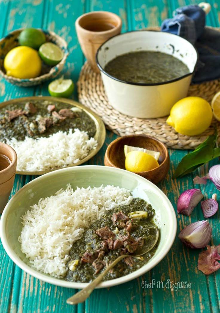 two bowls filled with rice and meat on top of a blue wooden table next to lemons