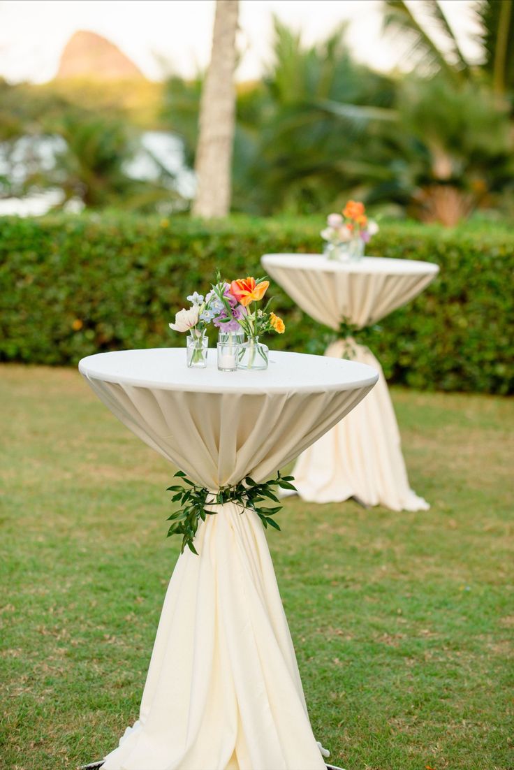 two tables with white cloths and flowers on them are set up in the grass