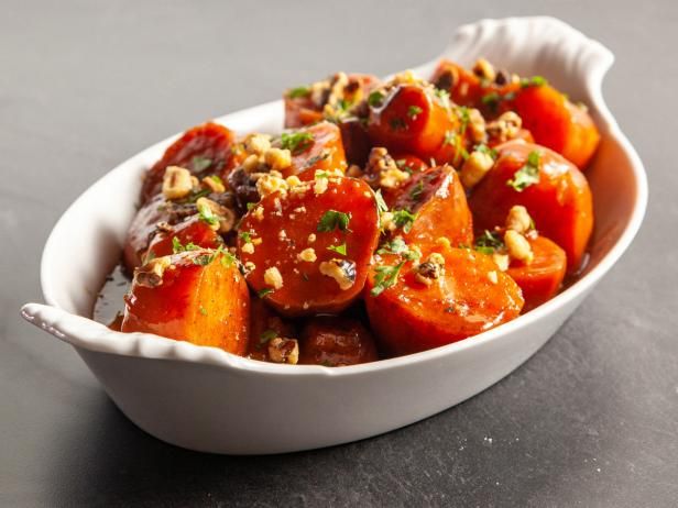 a white bowl filled with cooked carrots covered in sauce and garnished with chopped nuts