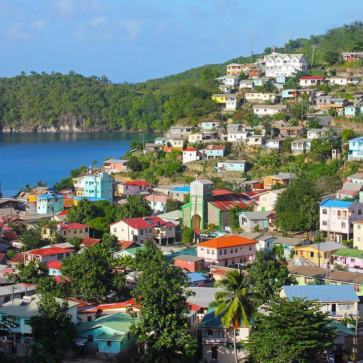 a city with lots of colorful houses on the hillside next to water and trees in front of it