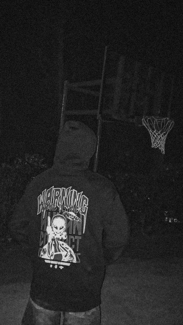 a man standing in front of a basketball hoop at night with his back to the camera