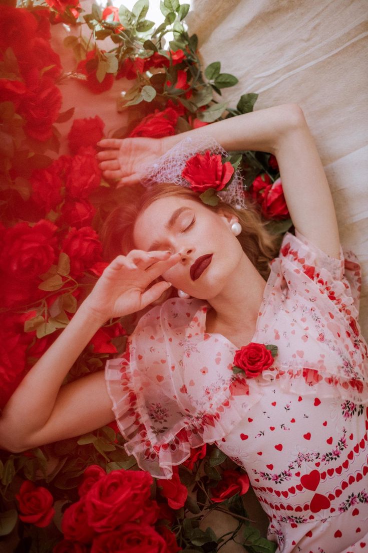 a woman laying on top of a bed covered in red flowers and greenery with her eyes closed