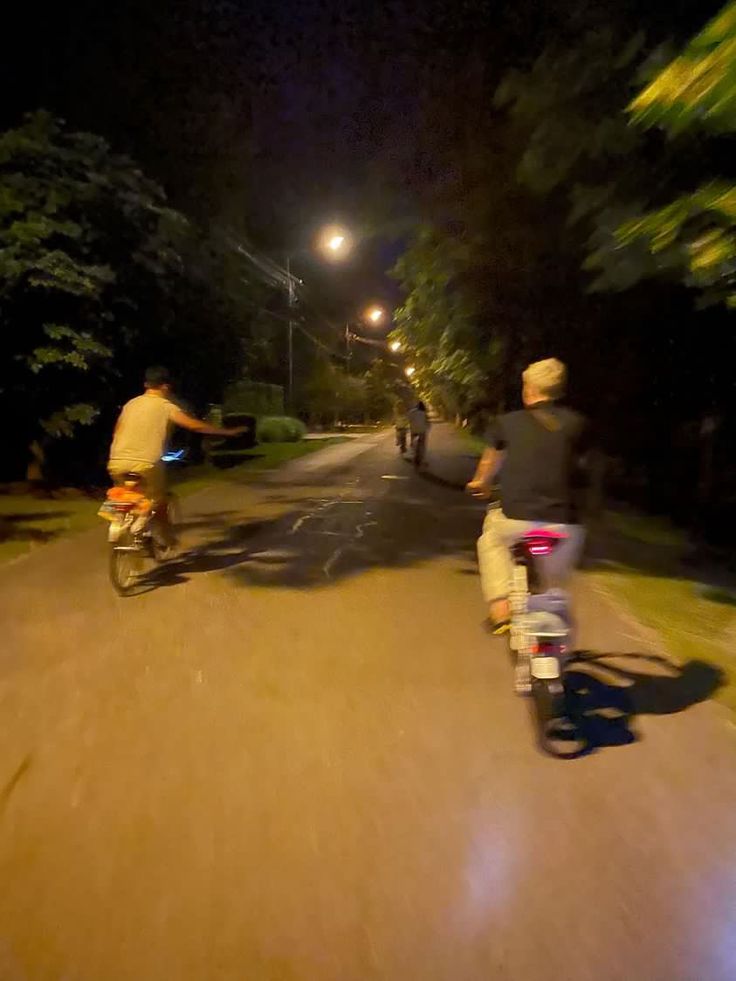 two people riding bikes down a street at night time with one person on the bike