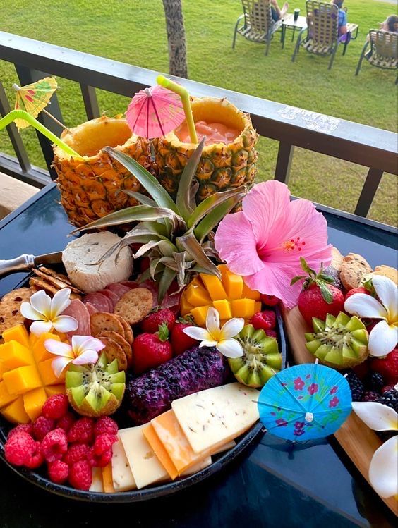 an assortment of fruits and cheeses on a table outside with people in the background