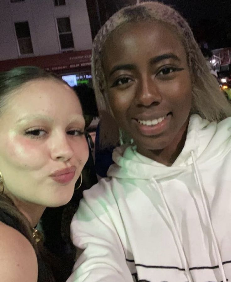 two women are taking a selfie in front of a building at night with bright lights