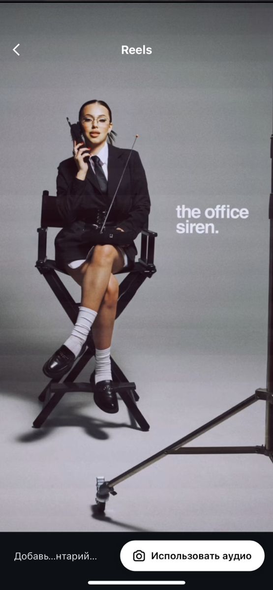 a woman sitting in a chair holding a cell phone to her ear while wearing a suit and tie