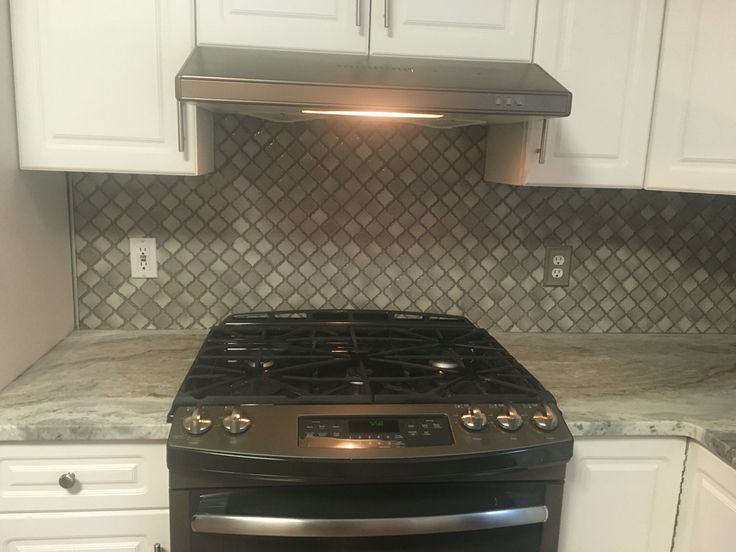 a stove top oven sitting inside of a kitchen next to white cabinets and counter tops