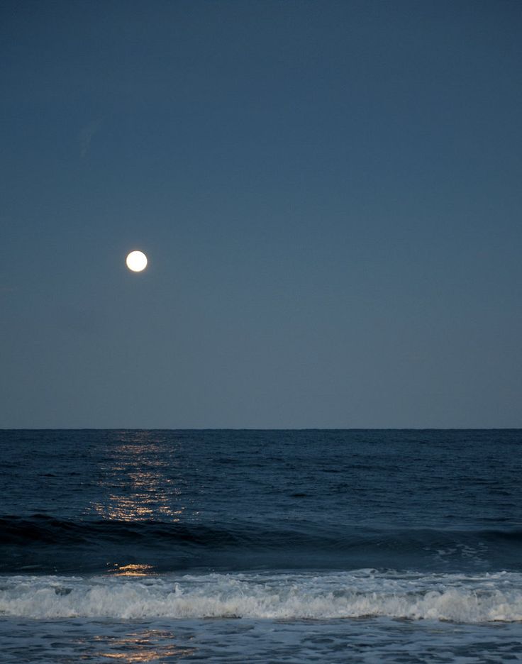 the moon is setting over the ocean with waves