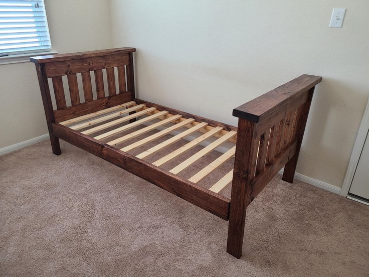 a bed frame made out of wood in a room with carpeted floor and white walls