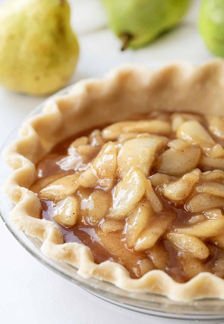 a pie crust with apples and pears in the background on a white countertop