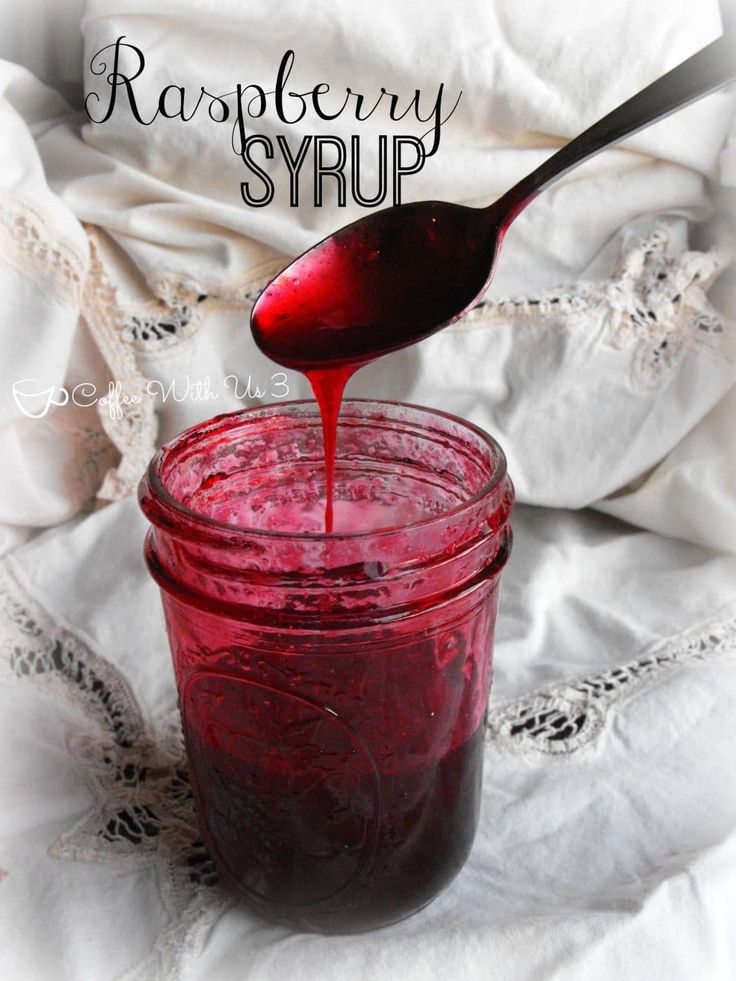 a spoon pouring red liquid into a glass jar on top of a white cloth covered tablecloth