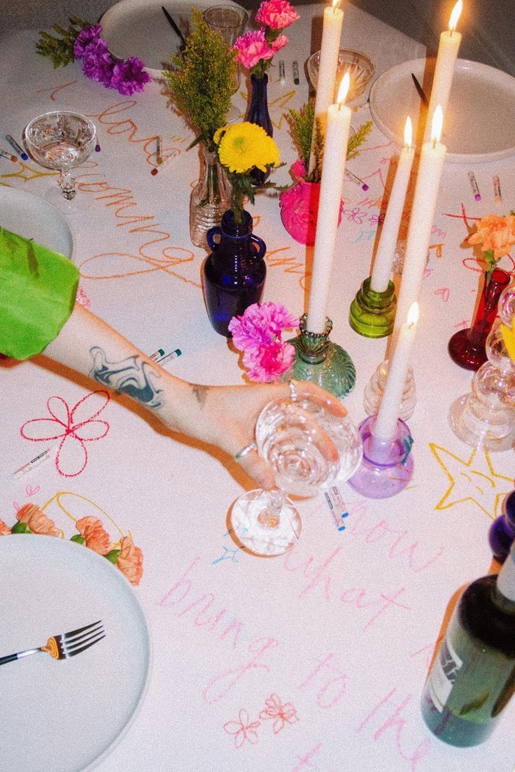 a table topped with lots of candles and plates covered in writing next to vases filled with flowers