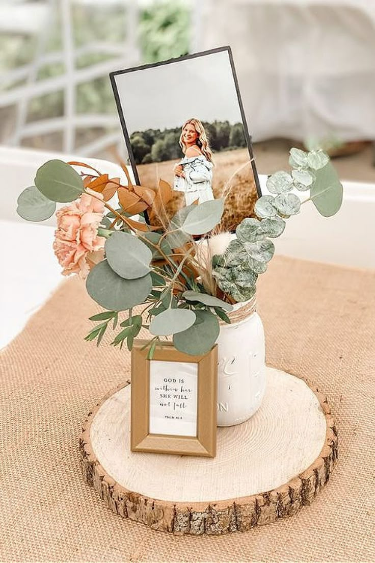 a vase filled with flowers and greenery on top of a wooden table next to a photo frame