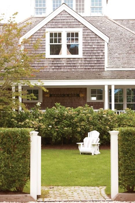 a white lawn chair sitting in front of a house next to a lush green yard