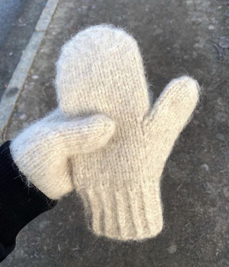 a person wearing a pair of white knitted mittens on their fingers and thumb